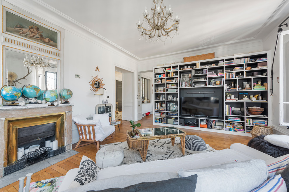 Idée de décoration pour une salle de séjour bohème fermée avec une bibliothèque ou un coin lecture, un mur blanc, un sol en bois brun, une cheminée standard et un téléviseur encastré.