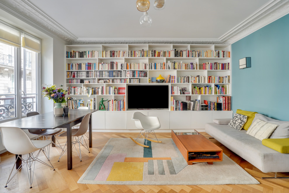 Foto de sala de estar con biblioteca cerrada actual de tamaño medio sin chimenea con paredes azules, suelo de madera clara, pared multimedia y suelo beige