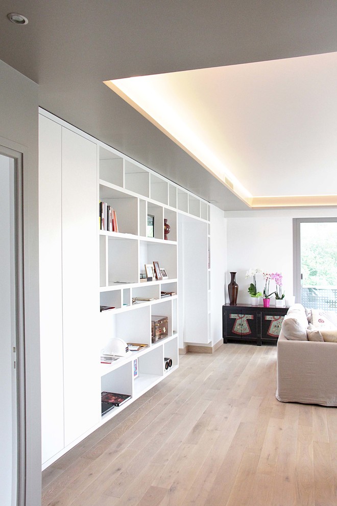Modelo de sala de estar con biblioteca abierta contemporánea grande sin televisor con paredes blancas y suelo de madera clara