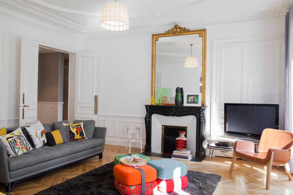パリにある高級な中くらいなトランジショナルスタイルのおしゃれな独立型ファミリールーム (白い壁、淡色無垢フローリング、標準型暖炉、石材の暖炉まわり、据え置き型テレビ) の写真