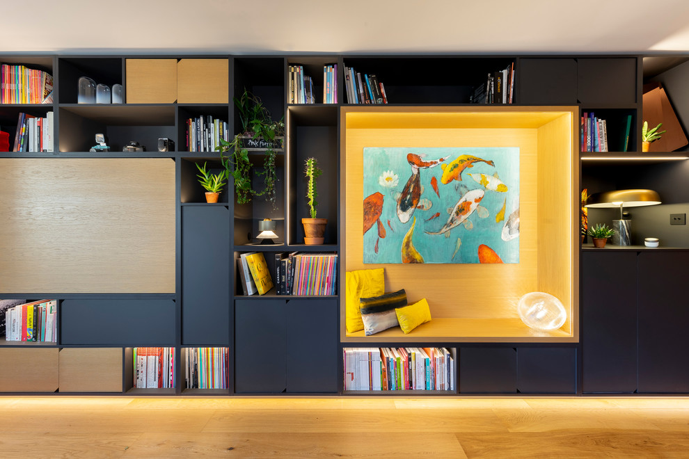 Cette image montre une grande salle de séjour minimaliste ouverte avec une bibliothèque ou un coin lecture, un mur blanc, parquet clair, un téléviseur dissimulé et un sol marron.