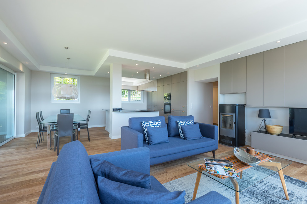 Inspiration pour une grande salle de séjour design ouverte avec un mur beige, un sol en contreplaqué, un poêle à bois, un téléviseur indépendant et un sol beige.
