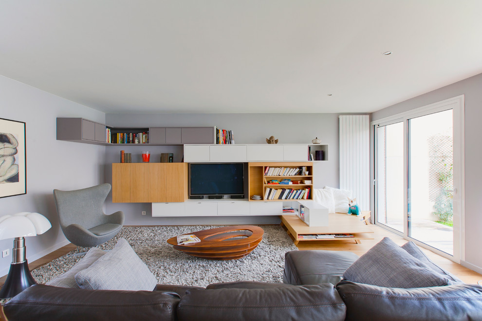 Immagine di un grande soggiorno design aperto con pareti grigie, parquet chiaro, nessun camino e TV nascosta