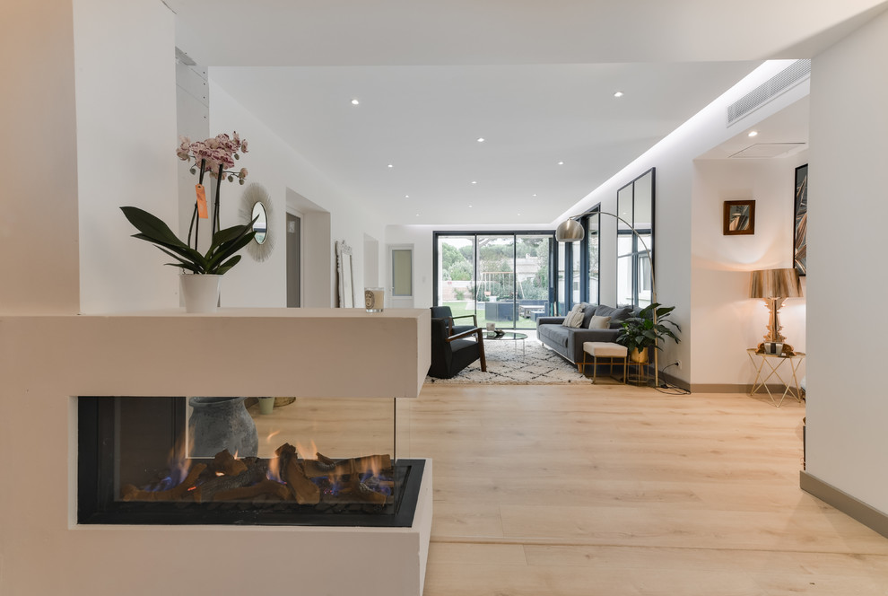 Design ideas for a large contemporary open plan games room in Montpellier with white walls, laminate floors, a two-sided fireplace, a plastered fireplace surround, no tv and beige floors.