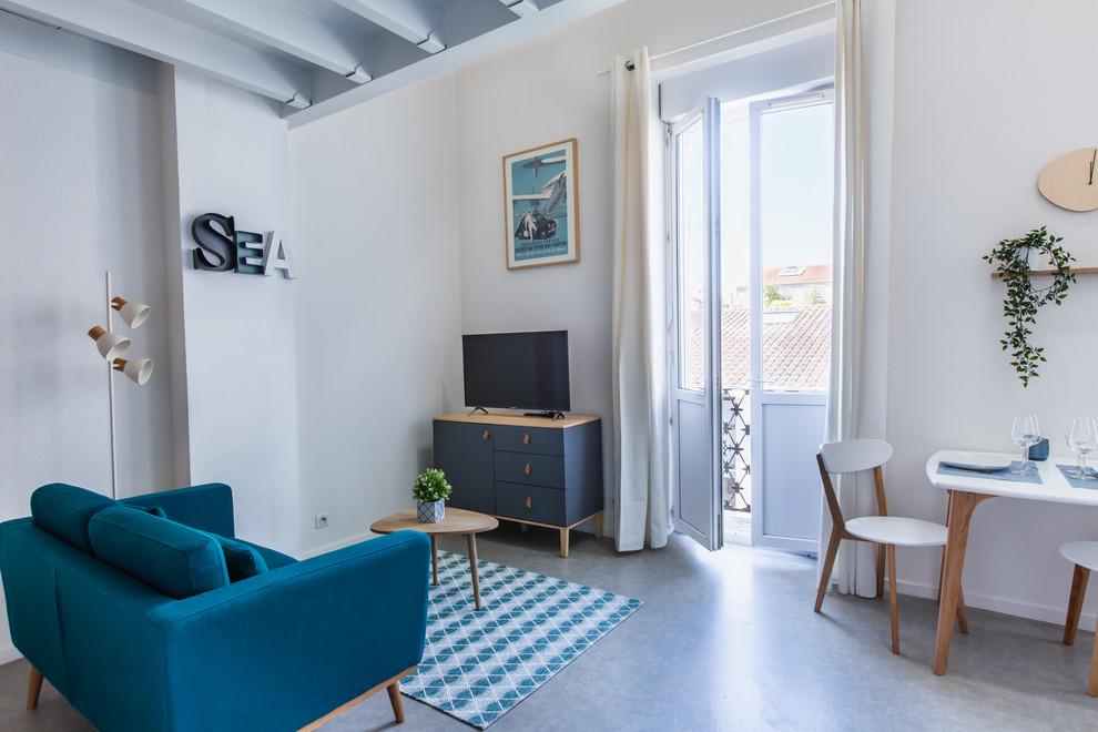 Свежая идея для дизайна: открытая гостиная комната среднего размера в морском стиле с белыми стенами, бетонным полом, отдельно стоящим телевизором и серым полом - отличное фото интерьера