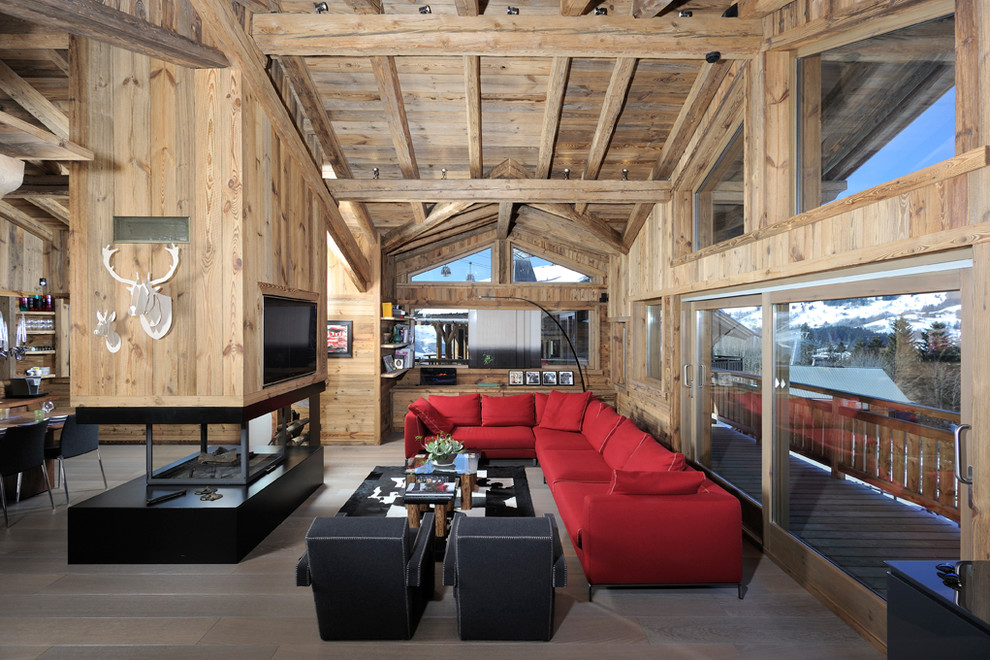Ejemplo de sala de estar abierta rústica grande con suelo de madera oscura, chimenea de doble cara, televisor colgado en la pared y marco de chimenea de metal