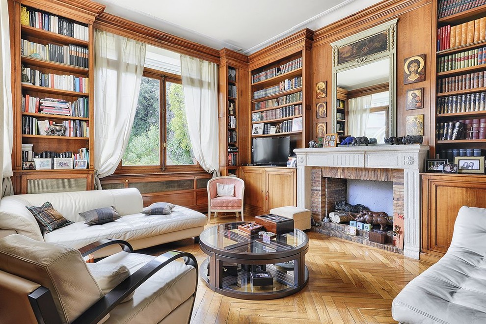 Cette photo montre une salle de séjour chic avec une bibliothèque ou un coin lecture, un mur marron, parquet clair, une cheminée standard, un manteau de cheminée en pierre, un téléviseur indépendant et un sol marron.