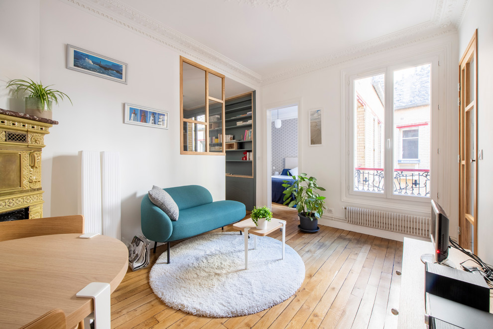 パリにあるお手頃価格の小さな北欧スタイルのおしゃれな独立型ファミリールーム (白い壁、無垢フローリング、コーナー設置型暖炉、石材の暖炉まわり、据え置き型テレビ、茶色い床) の写真