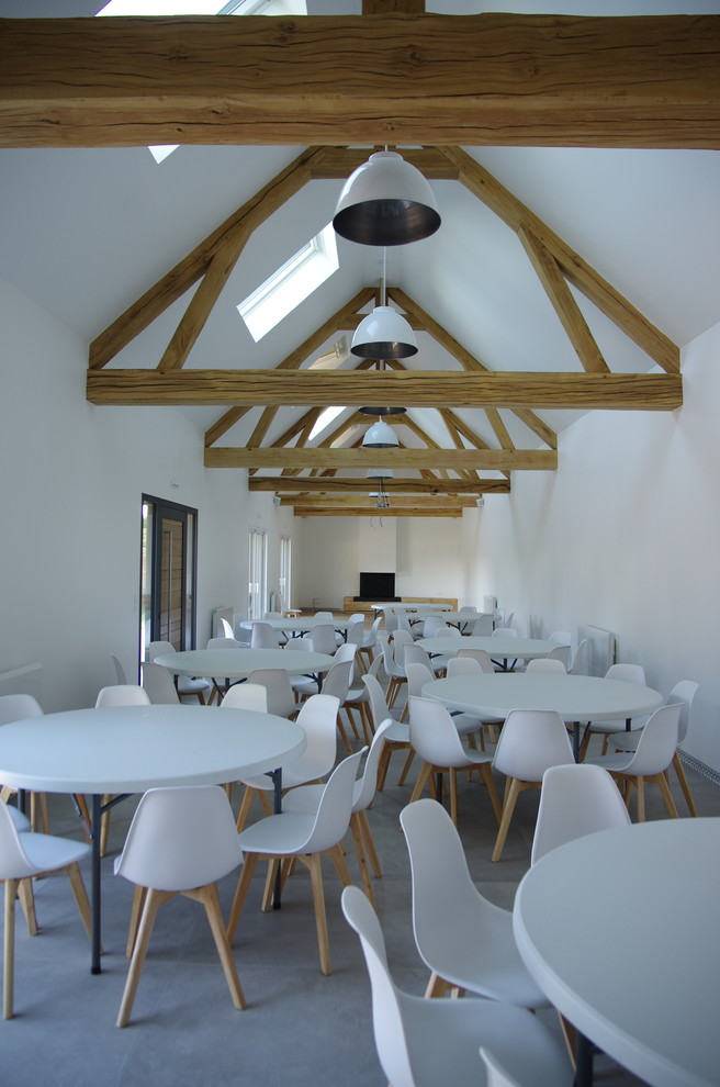 Cette image montre une grande salle à manger design avec un sol en carrelage de céramique, une cheminée standard, un manteau de cheminée en plâtre, un sol gris et un mur blanc.
