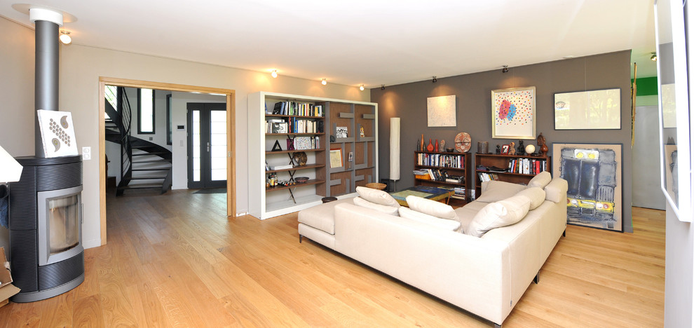 Cette photo montre une grande salle de séjour tendance ouverte avec un mur marron, parquet clair et une bibliothèque ou un coin lecture.
