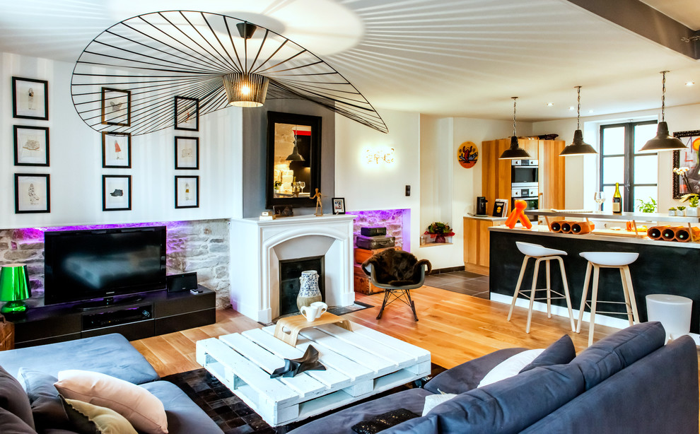Cette image montre une salle de séjour bohème ouverte et de taille moyenne avec une cheminée standard, un téléviseur indépendant, un mur blanc, un sol en bois brun et un manteau de cheminée en béton.