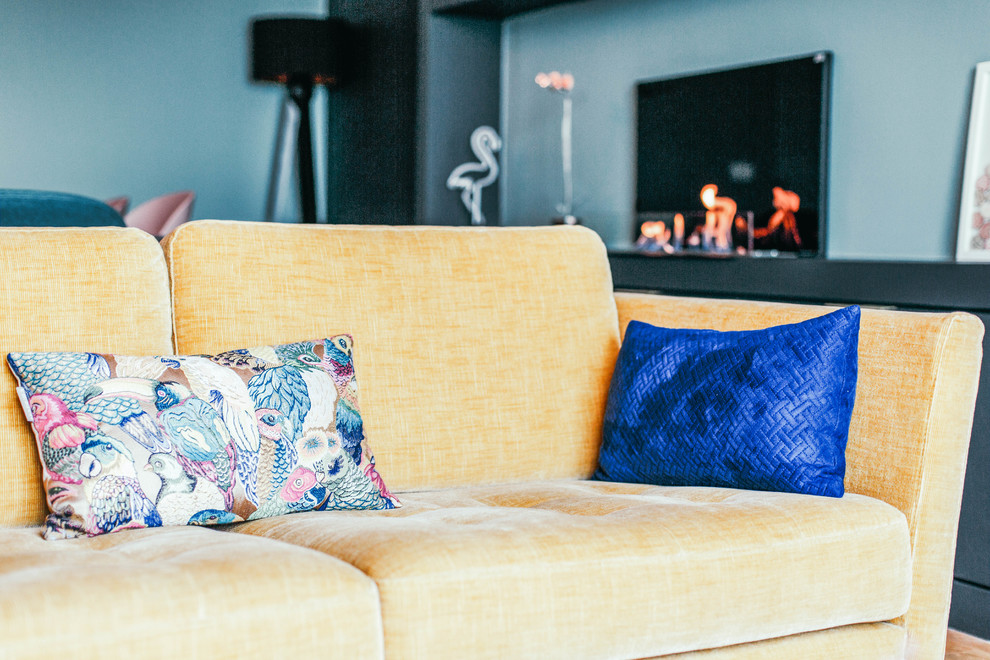 Diseño de sala de estar con biblioteca abierta contemporánea de tamaño medio con paredes azules, suelo de madera clara, todas las chimeneas, marco de chimenea de metal, televisor independiente y suelo beige