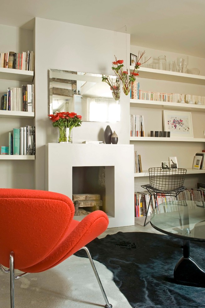 Cette photo montre une grande salle de séjour tendance ouverte avec une bibliothèque ou un coin lecture, un mur blanc, sol en béton ciré, une cheminée standard et un manteau de cheminée en béton.