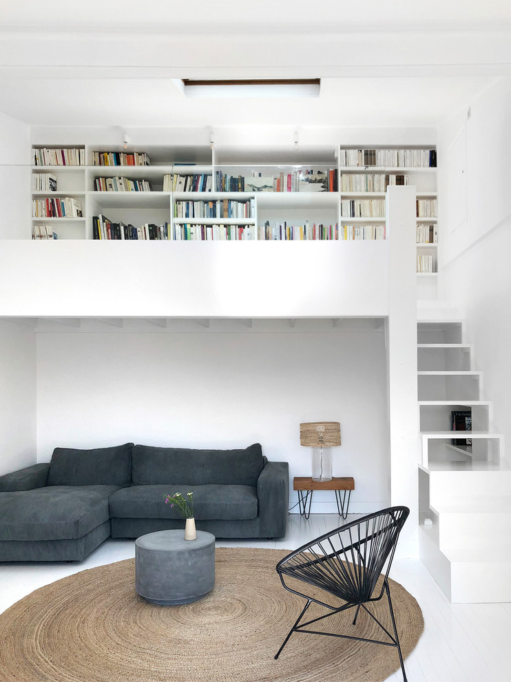 Идея дизайна: большая открытая гостиная комната в современном стиле с белыми стенами, деревянным полом, белым полом, с книжными шкафами и полками и ковром на полу без телевизора