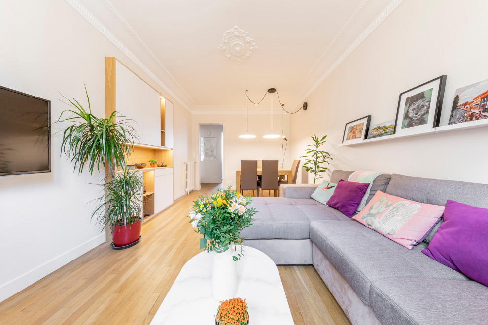 Imagen de sala de estar cerrada contemporánea pequeña sin chimenea con paredes beige, suelo de madera clara, televisor colgado en la pared y suelo beige