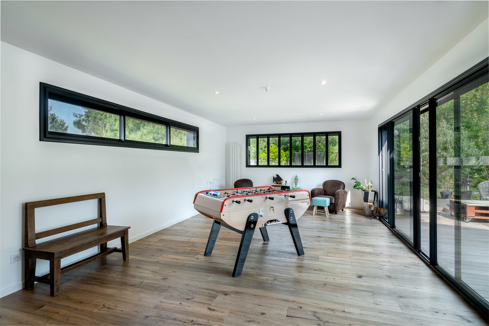 Imagen de sala de juegos en casa cerrada contemporánea con paredes blancas, suelo de madera en tonos medios y suelo marrón