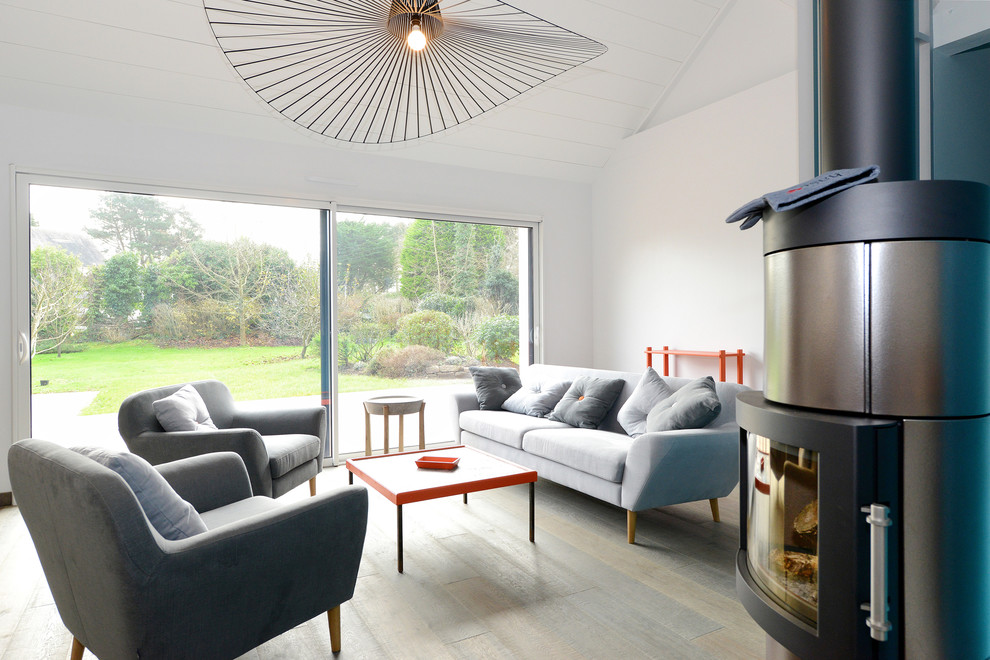 Modelo de sala de estar abierta contemporánea de tamaño medio sin televisor con paredes blancas, suelo de madera clara, estufa de leña y marco de chimenea de metal
