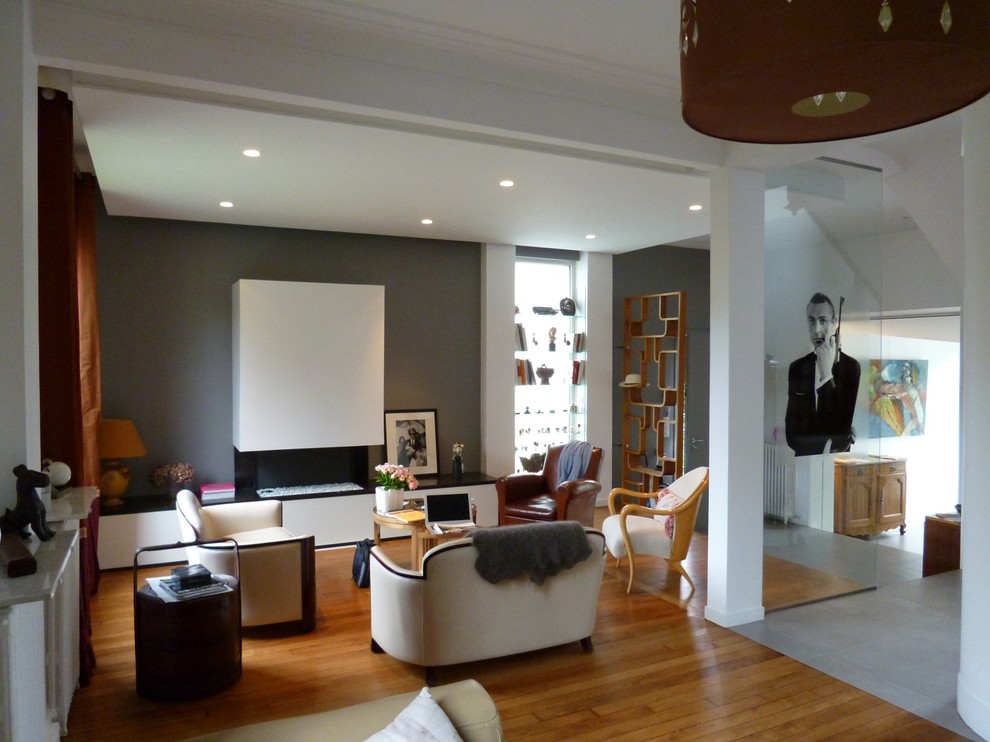 Ejemplo de sala de estar abierta contemporánea con paredes grises, suelo de madera clara, chimenea de esquina y marco de chimenea de piedra
