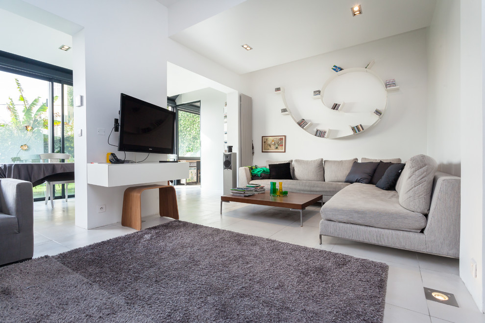 Пример оригинального дизайна: большая открытая гостиная комната в современном стиле с белыми стенами, телевизором на стене и полом из керамической плитки без камина