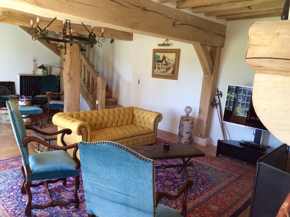 Aménagement d'une salle de séjour campagne ouverte avec un mur blanc, tomettes au sol, une cheminée standard, un manteau de cheminée en pierre, un téléviseur indépendant et un sol rouge.