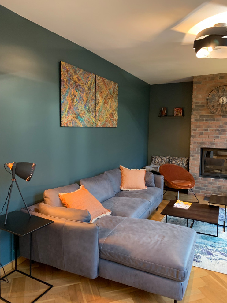 Diseño de sala de estar con biblioteca abierta industrial de tamaño medio con paredes azules, suelo laminado, todas las chimeneas, marco de chimenea de ladrillo, televisor colgado en la pared y suelo marrón