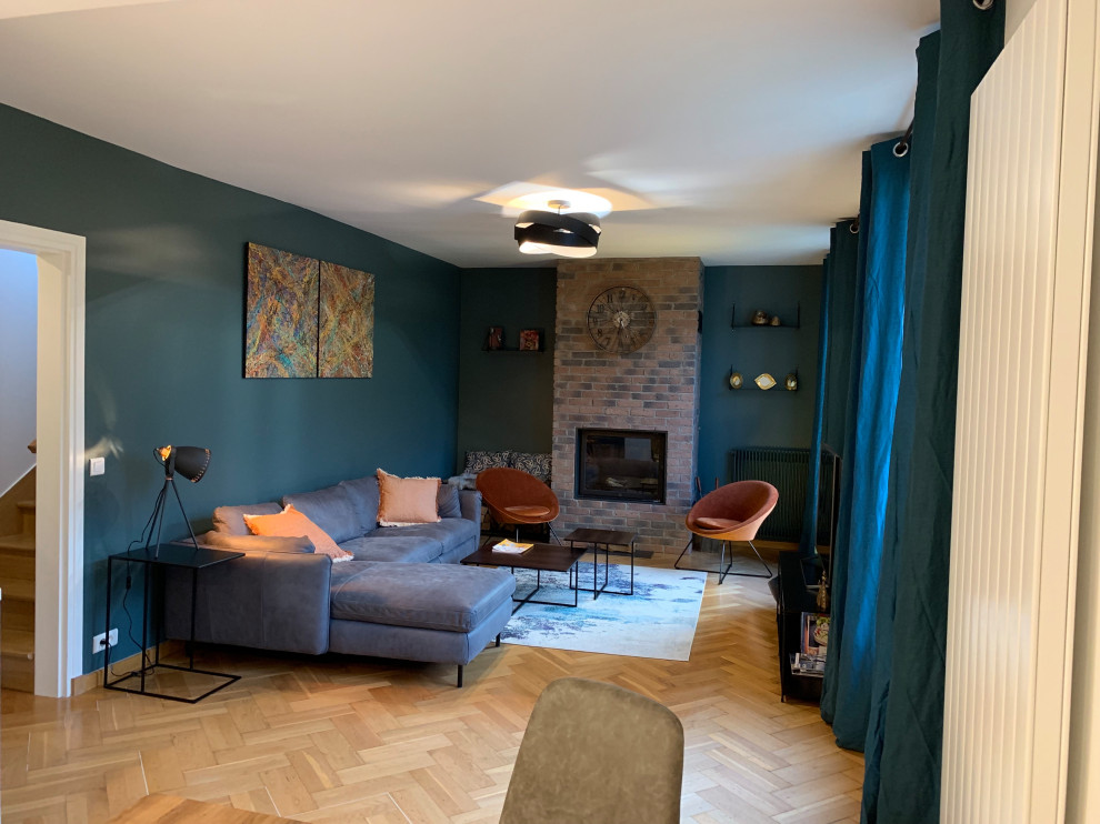 Imagen de sala de estar con biblioteca abierta industrial de tamaño medio con paredes azules, suelo laminado, todas las chimeneas, marco de chimenea de ladrillo, televisor colgado en la pared y suelo marrón
