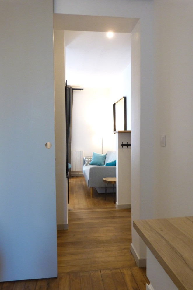 Cette photo montre une petite salle de séjour industrielle ouverte avec un mur blanc et un sol en bois brun.