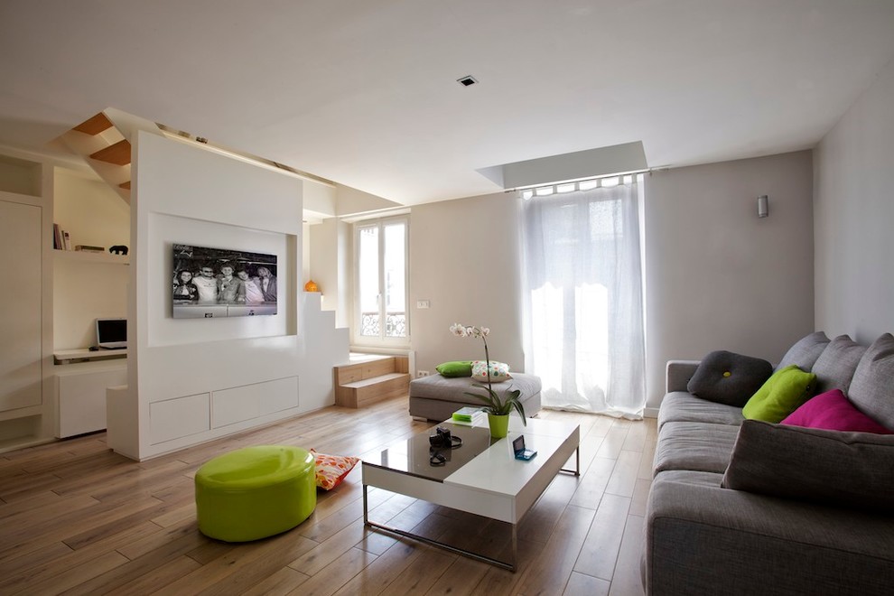 Modelo de sala de estar cerrada actual de tamaño medio sin chimenea con paredes grises, suelo de madera oscura, televisor colgado en la pared y suelo marrón