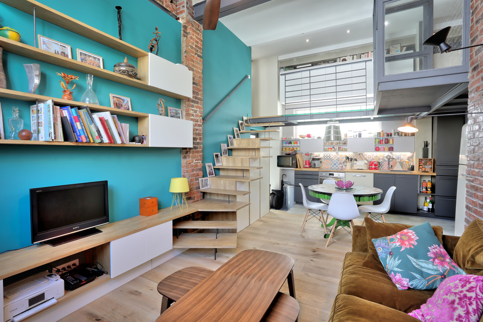 Imagen de sala de estar abierta industrial pequeña con paredes verdes, suelo de madera clara, televisor independiente y suelo marrón