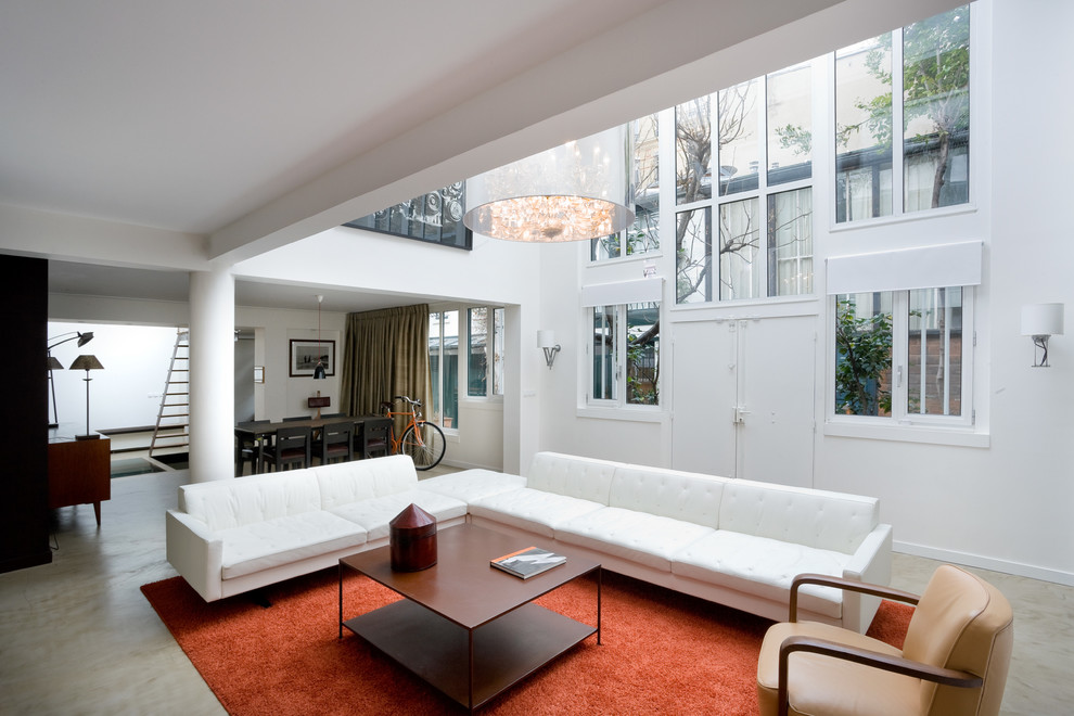 На фото: большая открытая гостиная комната в современном стиле с белыми стенами и бетонным полом с