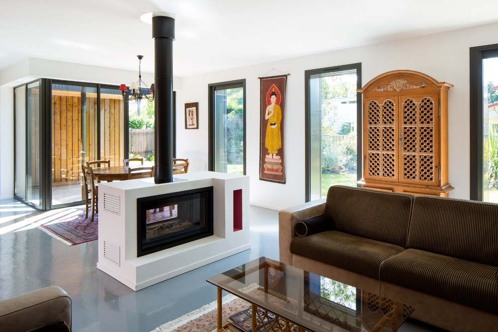 Modelo de sala de estar abierta contemporánea con paredes blancas, chimenea de doble cara y suelo gris