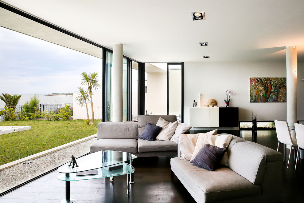 Modelo de sala de estar abierta contemporánea grande sin televisor con paredes blancas y suelo de madera oscura