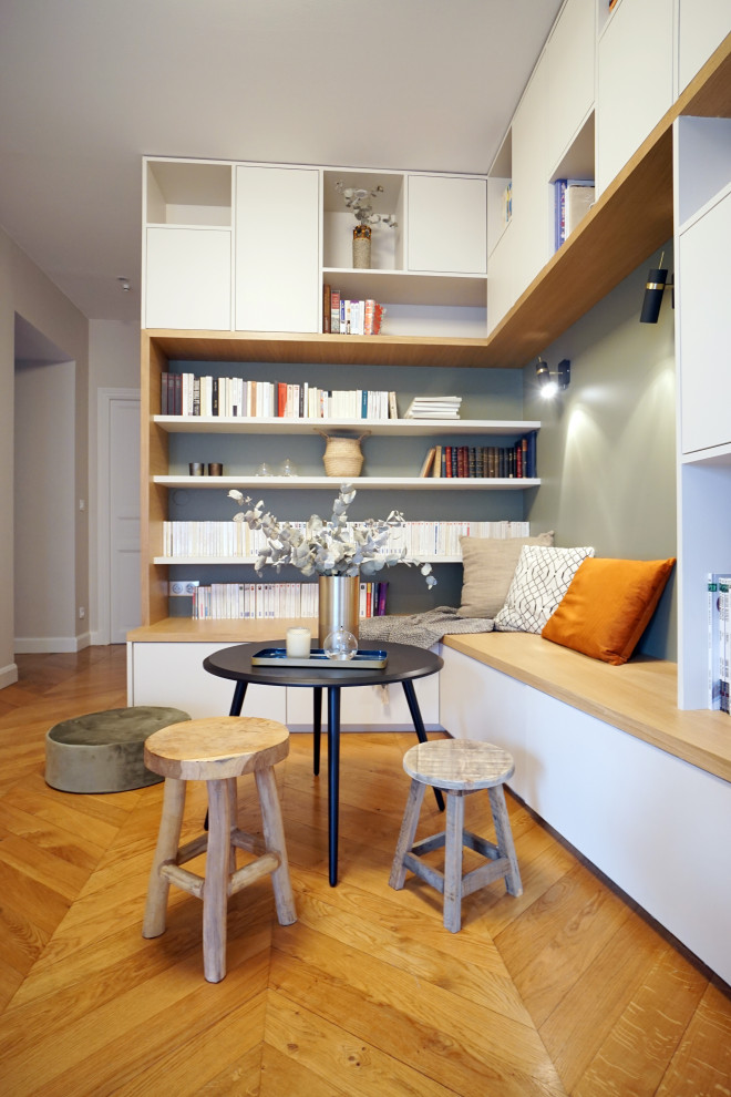 Ispirazione per un soggiorno design di medie dimensioni e aperto con libreria, pareti grigie, pavimento in legno massello medio, nessuna TV e pavimento beige