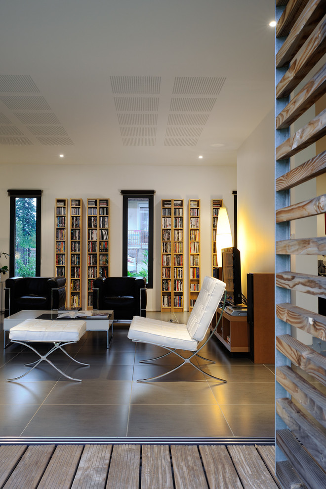 Inredning av ett modernt stort allrum med öppen planlösning, med ett bibliotek, vita väggar, klinkergolv i keramik och en fristående TV