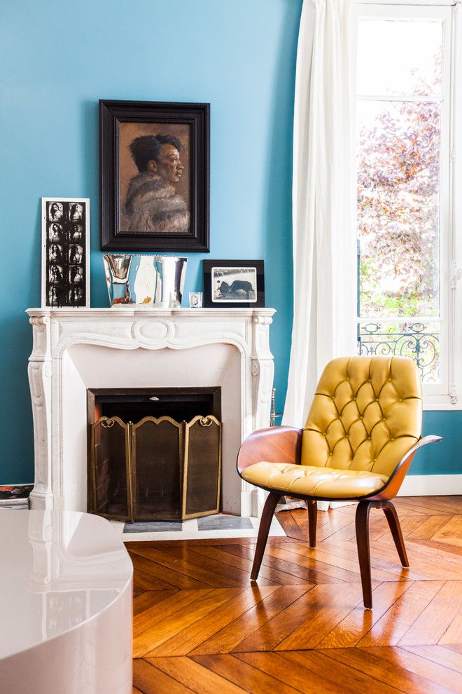 Mittelgroßes, Fernseherloses, Offenes Modernes Wohnzimmer mit blauer Wandfarbe, braunem Holzboden, Kamin und Kaminumrandung aus Stein in Paris