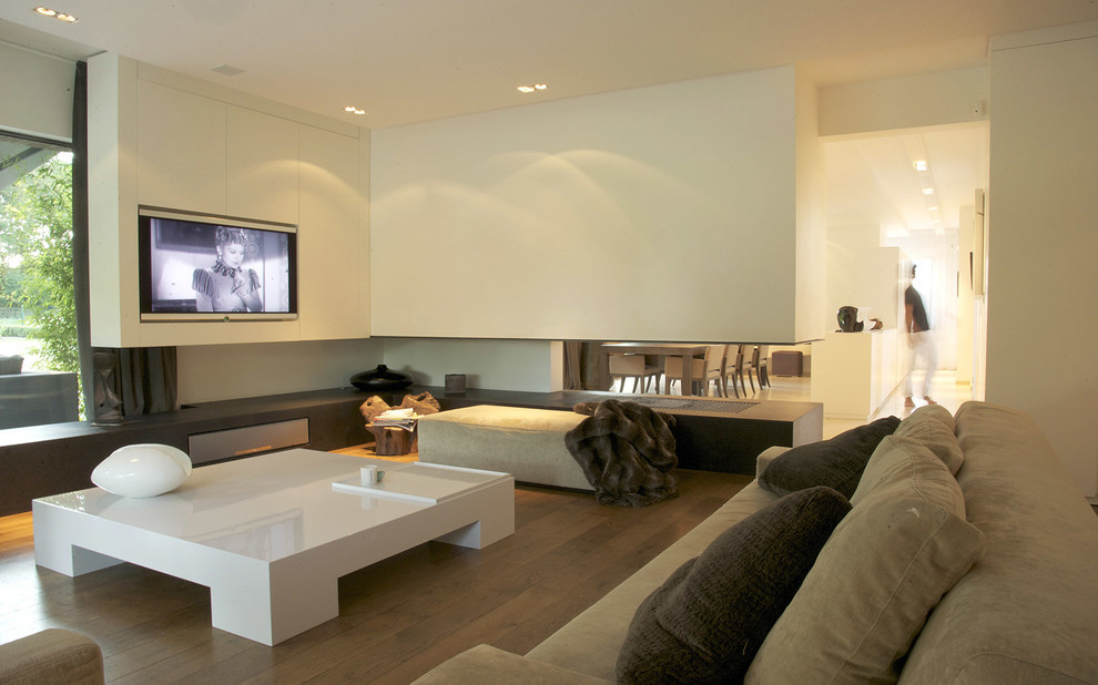 Imagen de sala de estar abierta tradicional de tamaño medio con paredes blancas, suelo de madera en tonos medios, chimenea de doble cara y pared multimedia