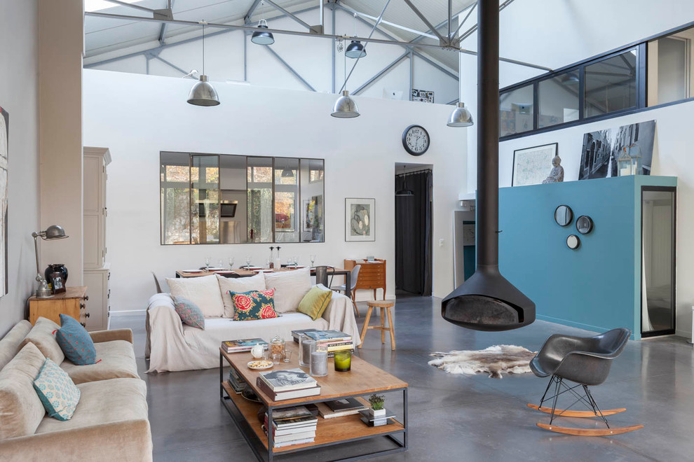 Inspiration for a large industrial open concept concrete floor and gray floor family room remodel in Paris with white walls, a hanging fireplace and a metal fireplace
