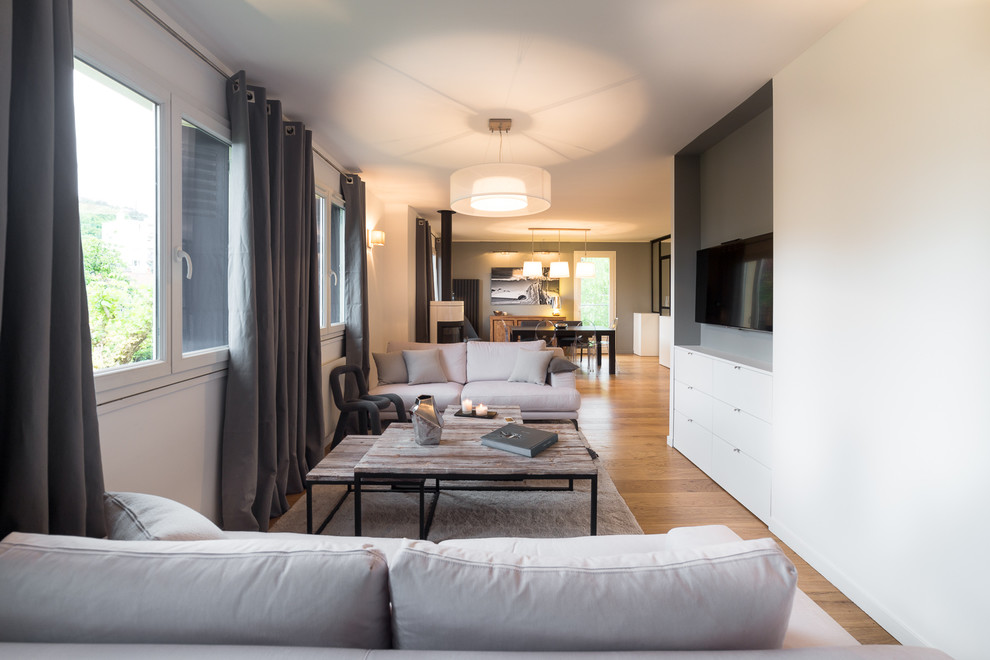 Ejemplo de sala de estar abierta actual de tamaño medio con paredes blancas, suelo de madera en tonos medios y pared multimedia