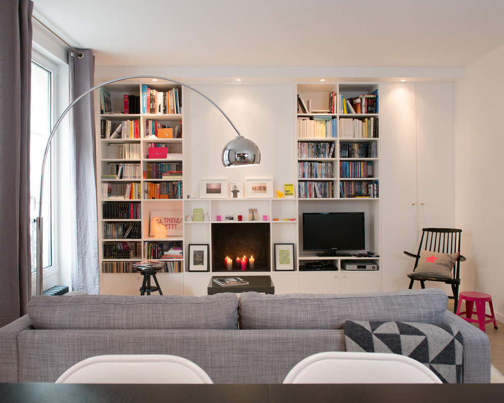 На фото: открытая гостиная комната в скандинавском стиле с с книжными шкафами и полками, белыми стенами и отдельно стоящим телевизором без камина