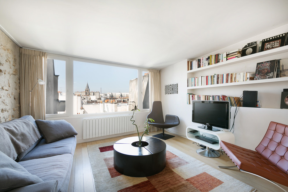 Imagen de sala de estar con biblioteca cerrada contemporánea de tamaño medio sin chimenea con paredes blancas, suelo de madera clara y televisor independiente