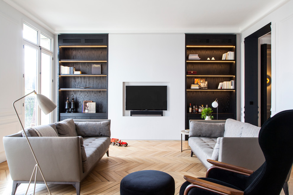 Modelo de sala de estar abierta actual grande sin chimenea con paredes blancas, suelo de madera clara, pared multimedia y suelo beige