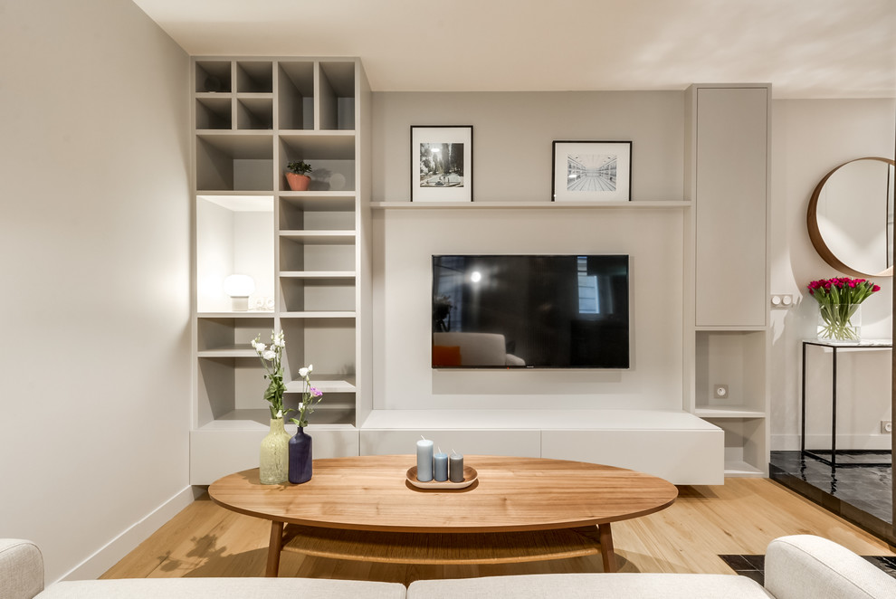 Пример оригинального дизайна: открытая гостиная комната среднего размера в современном стиле с с книжными шкафами и полками, серыми стенами, светлым паркетным полом и телевизором на стене без камина