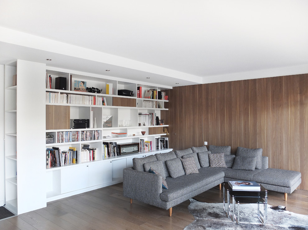 Modelo de sala de estar con biblioteca abierta contemporánea de tamaño medio sin chimenea y televisor con paredes blancas y suelo de madera clara