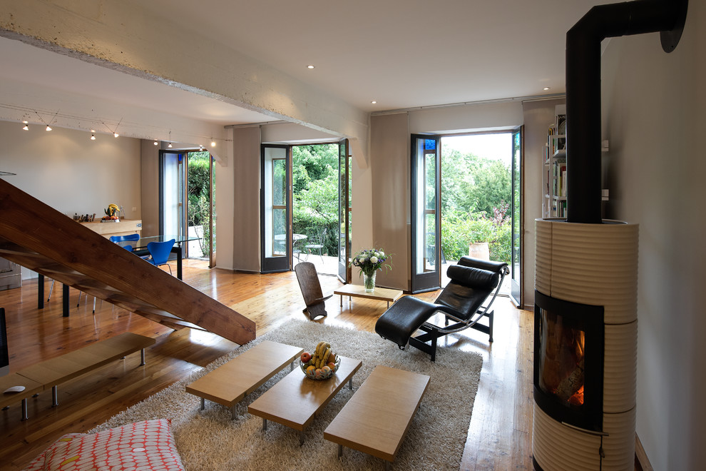 Modelo de sala de estar abierta actual grande sin televisor con paredes blancas y suelo de madera en tonos medios