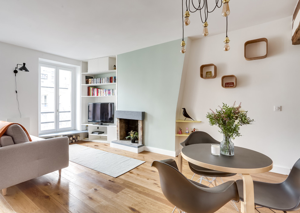 На фото: открытая гостиная комната в скандинавском стиле с белыми стенами, паркетным полом среднего тона, стандартным камином, отдельно стоящим телевизором и коричневым полом