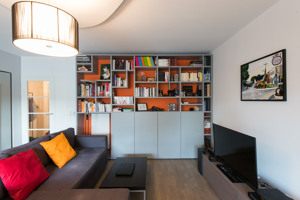 Cette image montre une grande salle de séjour design ouverte avec une bibliothèque ou un coin lecture, un mur orange, parquet clair, un téléviseur indépendant et aucune cheminée.