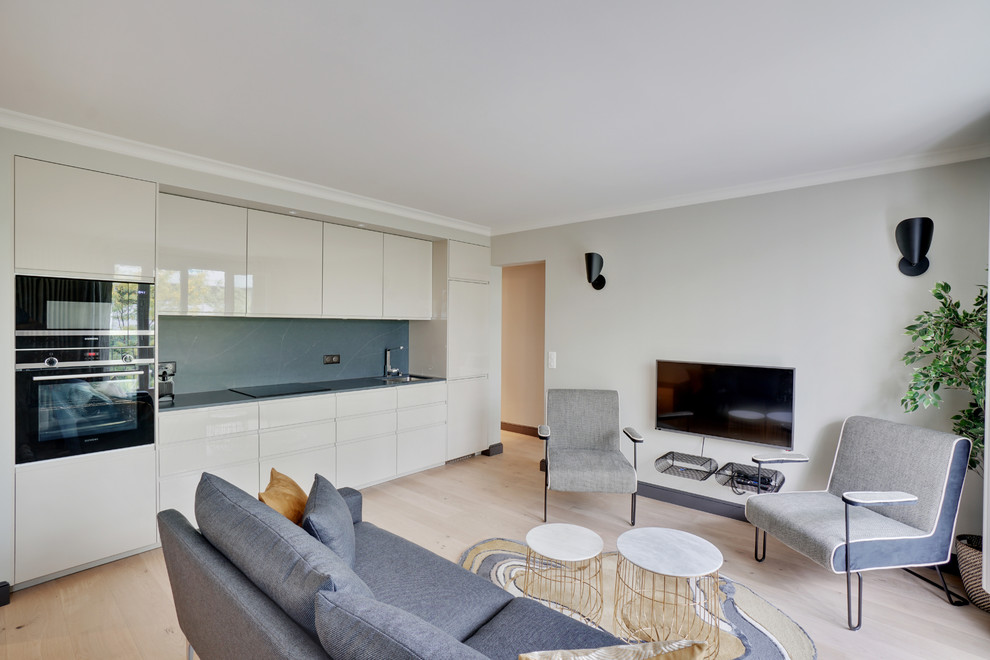 Foto de sala de estar abierta contemporánea pequeña con paredes grises, suelo de madera clara, televisor colgado en la pared y suelo beige