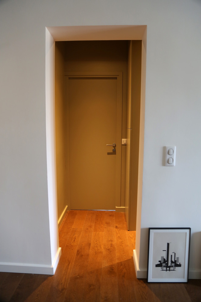 Modelo de sala de estar abierta actual de tamaño medio con paredes blancas, suelo de madera oscura y pared multimedia