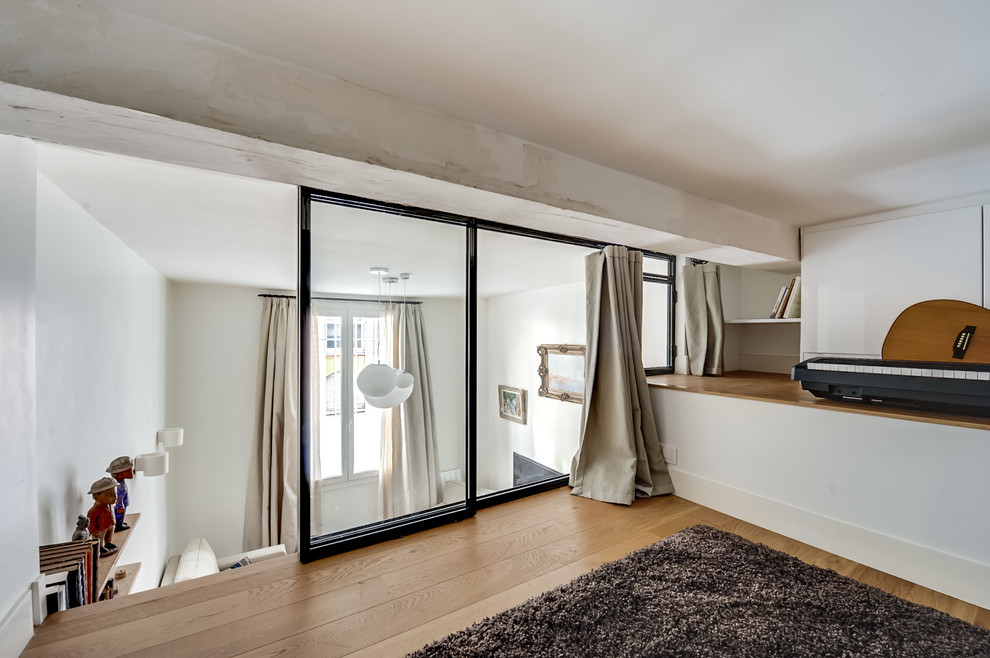 Cette photo montre une petite salle de séjour mansardée ou avec mezzanine tendance avec une salle de musique, un mur blanc, parquet clair et un sol beige.