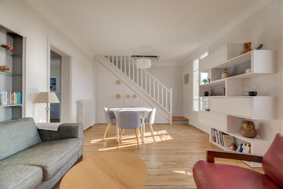 Cette photo montre une salle de séjour chic de taille moyenne avec un mur gris, parquet clair, une cheminée standard, un manteau de cheminée en pierre et un sol marron.